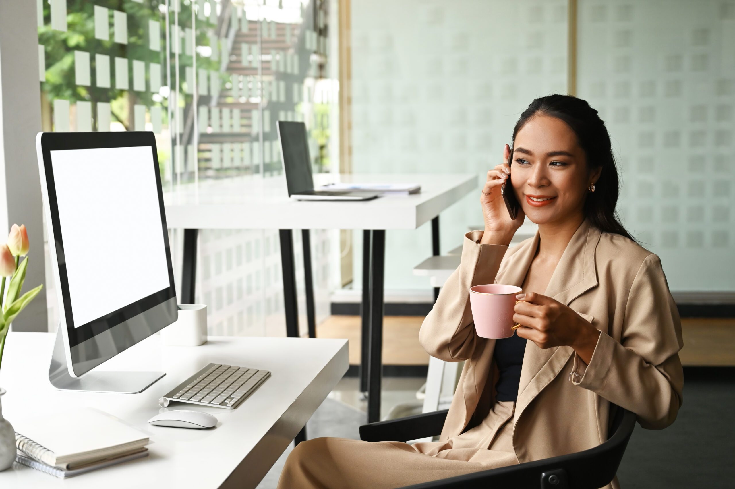 image holding cup of coffee while on the phone looking at her computer screen