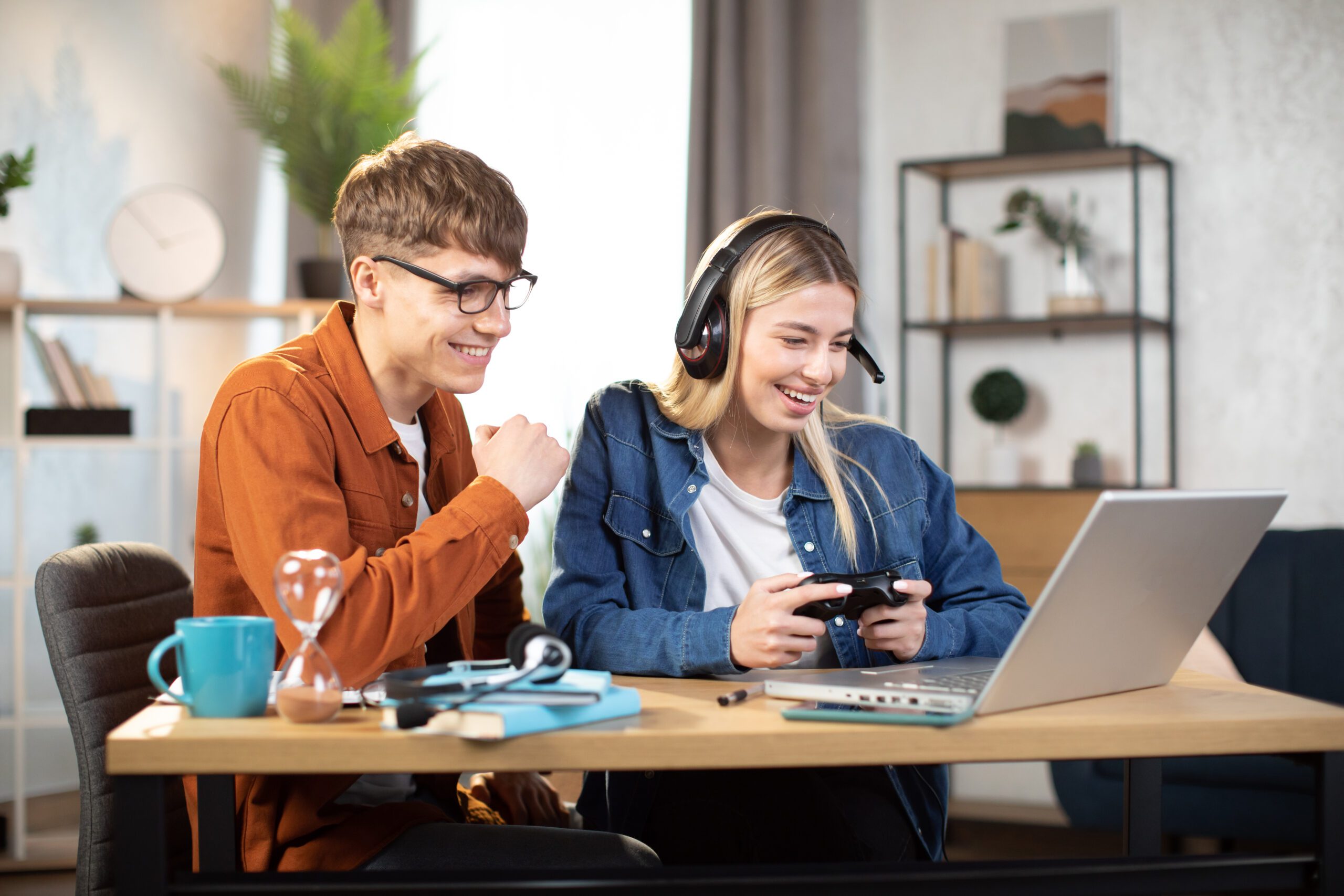 Happy young people enjoying video game, using gaming laptop and joystick